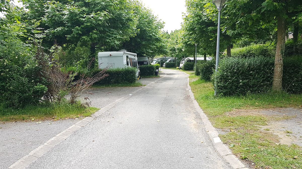 Área de autocaravanas arbolada con una autocaravana aparcada al fondo