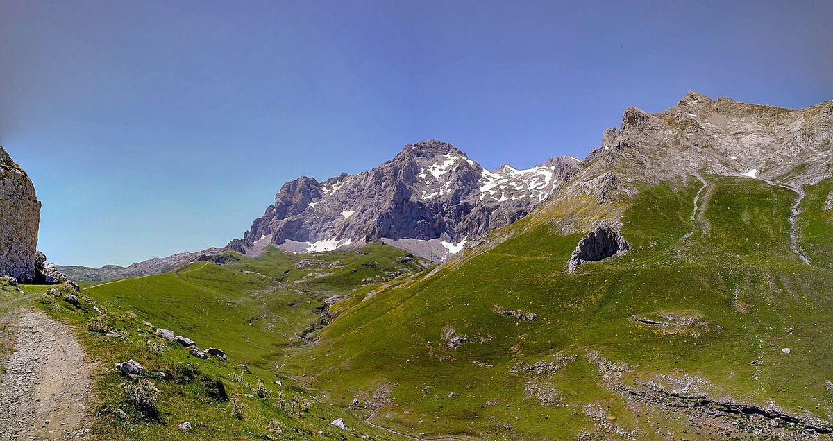 Valle verde de montaña con una pista entre cumbres calizas en los Picos de Europa